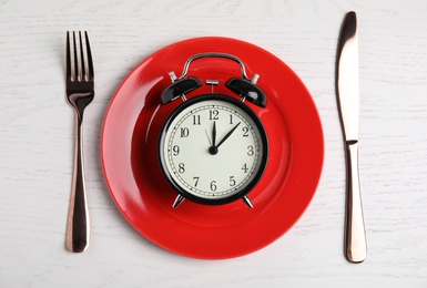 Alarm clock, plate and cutlery on white wooden table, flat lay. Diet regime