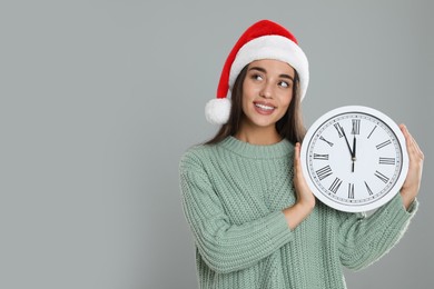 Photo of Woman in Santa hat with clock on grey background, space for text. New Year countdown
