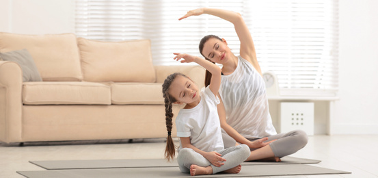 Young mother with little daughter practicing yoga at home. Banner design