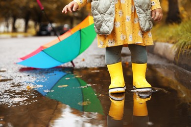Little girl wearing yellow rubber boots standing in puddle outdoors, closeup. Space for text