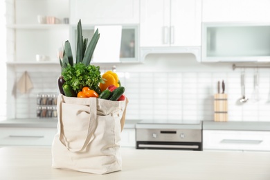 Textile shopping bag full of vegetables on table in kitchen. Space for text