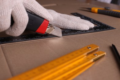 Worker cutting cardboard with utility knife and ruler, closeup