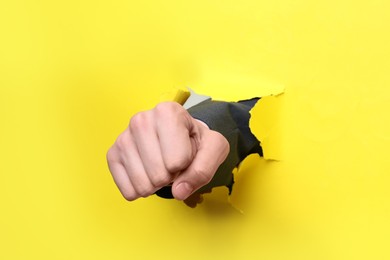Businessman breaking through yellow paper with fist, closeup