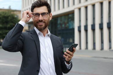 Handsome businessman with smartphone on city street, space for text
