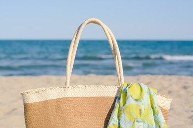 Straw bag with beach wrap on sandy seashore, closeup. Summer accessories