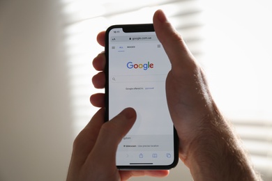 MYKOLAIV, UKRAINE - OCTOBER 27, 2020: Man using Google search engine on smartphone against blurred background, closeup