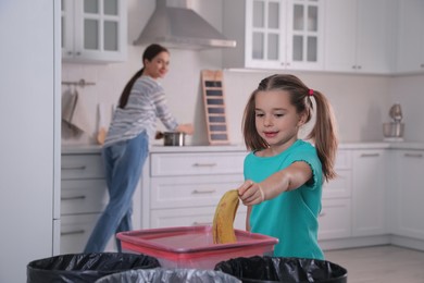Little girl throwing banana peel into trash bin in kitchen. Separate waste collection