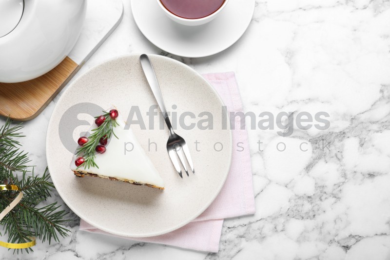 Photo of Slice of traditional Christmas cake decorated with rosemary and pomegranate seeds served on white marble table, flat lay. Space for text