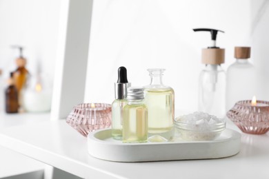 Essential oils, candles and sea salt on white shelf in bathroom