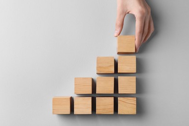 Photo of Woman holding wooden cube near others on light background, top view. Management concept