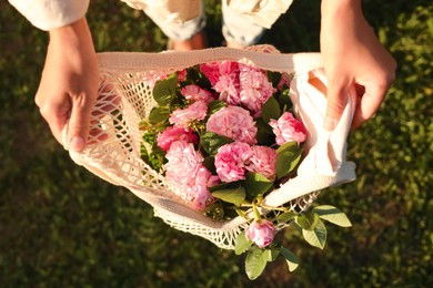 Photo of Woman holding mesh bag with beautiful tea roses outdoors, top view