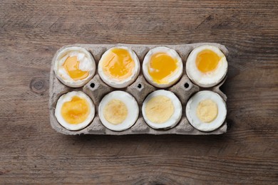 Photo of Boiled chicken eggs of different readiness stages in carton on wooden table, top view