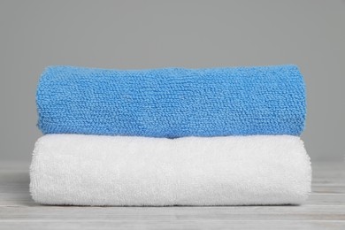 Soft folded towels on white wooden table against light grey background