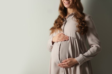 Pregnant woman touching her belly on light grey background, closeup. Space for text
