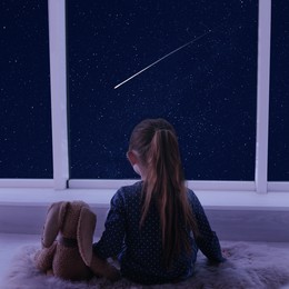 Image of Little girl near window looking at shooting star in beautiful night sky