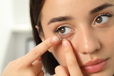 Woman putting contact lens in her eye on blurred background, closeup