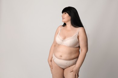 Beautiful overweight woman in beige underwear on light background, space for text. Plus-size model