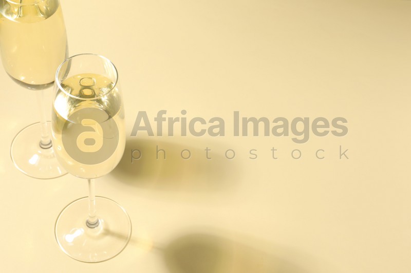 Photo of Glasses of delicious sparkling wine on light yellow background. Space for text