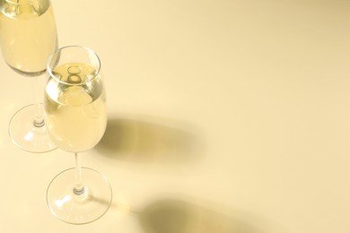 Photo of Glasses of delicious sparkling wine on light yellow background. Space for text