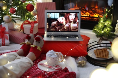MYKOLAIV, UKRAINE - DECEMBER 23, 2020: Woman watching The Queen's Gambit series on laptop near fireplace at home, closeup. Cozy winter holidays atmosphere