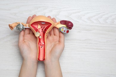 Woman with anatomical model of uterus at white wooden table, top view and space for text. Gynecology concept