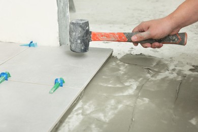 Worker with rubber hummer installing tiles indoors , closeup