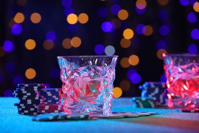 Alcohol drink, playing cards and casino chips on table against blurred lights