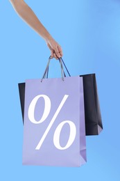 Woman holding paper shopping bag with percent sign on light blue background, closeup. Discount concept