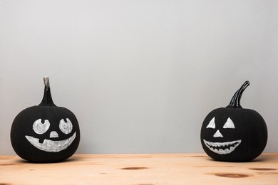 Halloween celebration. Black pumpkins with drawn spooky faces on wooden table, space for text