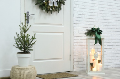 Beautiful Christmas lantern and potted fir tree near entrance indoors