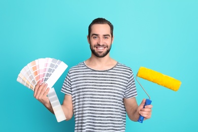 Young man with palette and roller on color background