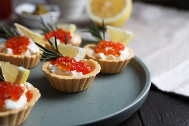 Photo of Delicious tartlets with red caviar and cream cheese served on wooden table, closeup. Space for text
