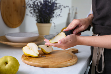 Woman cutting fresh ripe pear at table in kitchen, closeup