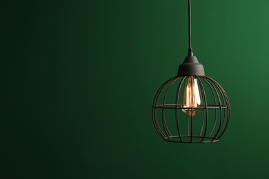 Hanging lamp bulb in chandelier against green background, space for text