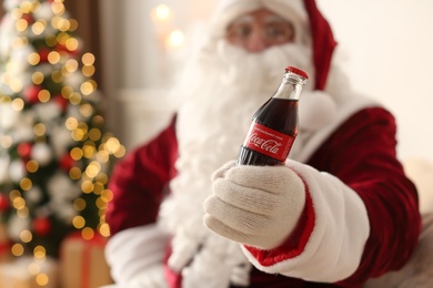 MYKOLAIV, UKRAINE - JANUARY 18, 2021: Santa Claus with Coca-Cola bottle in room decorated for Christmas, focus on hand