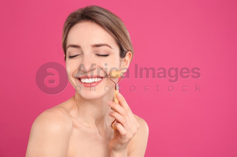 Photo of Young woman using natural jade face roller on pink background, space for text