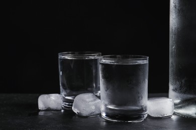 Vodka in shot glasses with ice on table against black background