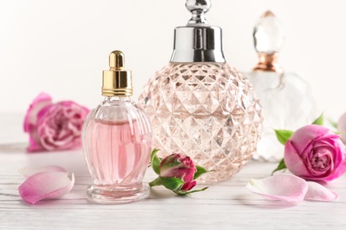 Different bottles of perfume and flowers on light background, closeup