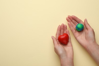 Woman holding model of planet and red heart on beige background, top view with space for text. Earth Day