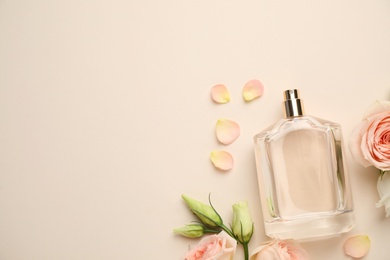 Flat lay composition of bottle with perfume and fresh flowers on beige background, space for text