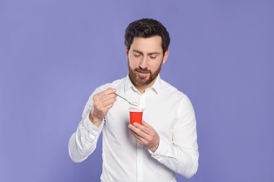 Photo of Handsome man with delicious yogurt and spoon on violet background