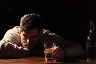 Addicted man with alcoholic drink at wooden table against black background, focus on glass