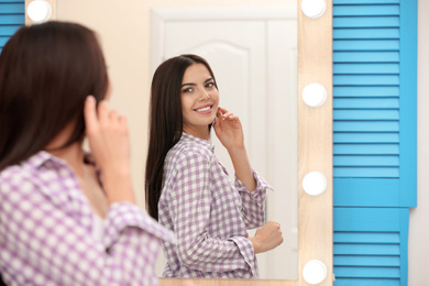 Young attractive woman looking at herself in stylish mirror at home