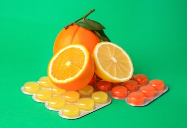 Photo of Blisters with cough drops and fresh fruits on green background