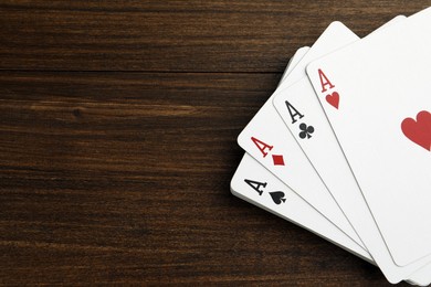 Four aces playing cards on wooden table, top view. Space for text