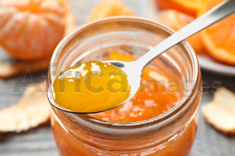 Photo of Teaspoon with tasty tangerine jam over jar, closeup