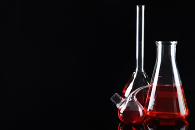 Laboratory glassware with colorful liquids on black background. Space for text