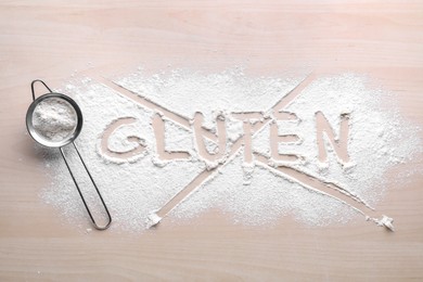Photo of Sifter and crossed out word Gluten written with flour on wooden table, top view