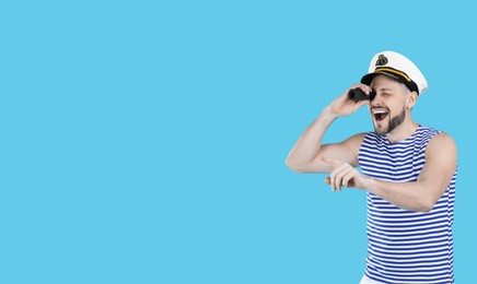 Sailor looking through monocular and pointing on light blue background