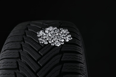 Winter tire with icy snowflake on black background, closeup